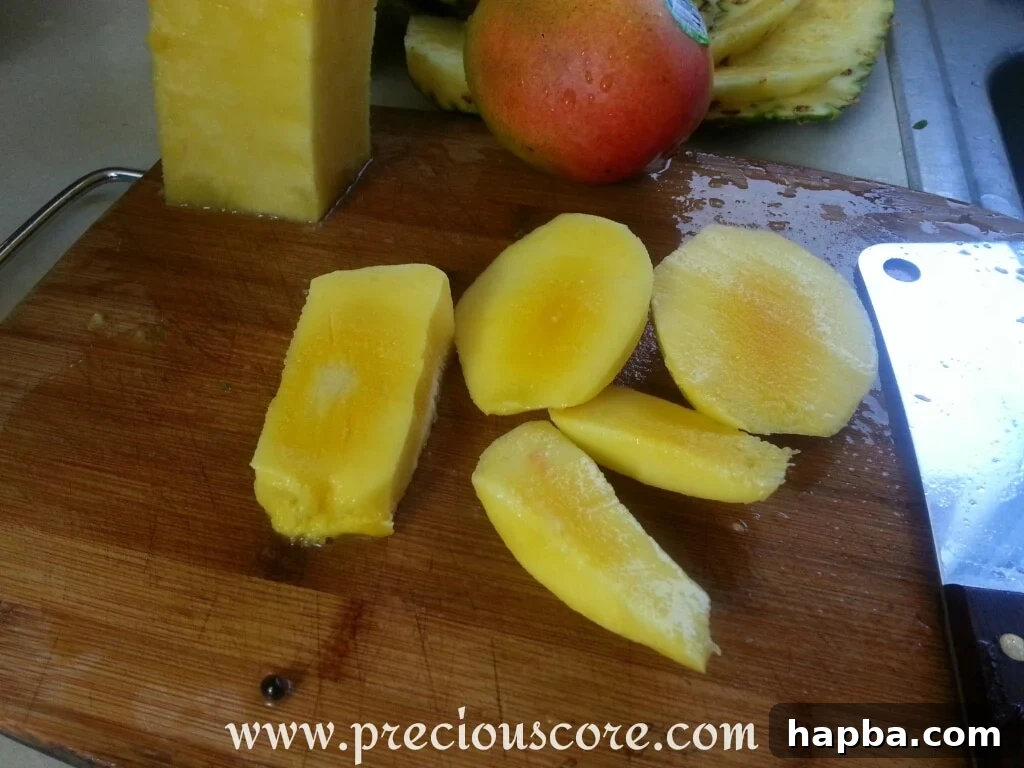 Freshly diced mango pieces, bright orange and juicy, added to a large mixing bowl already containing pineapple and papaya chunks.