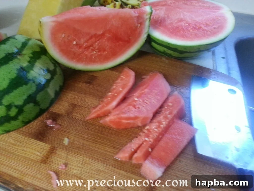 Diced watermelon pieces, bright red and seedless, being added to the communal bowl of mixed tropical fruits.