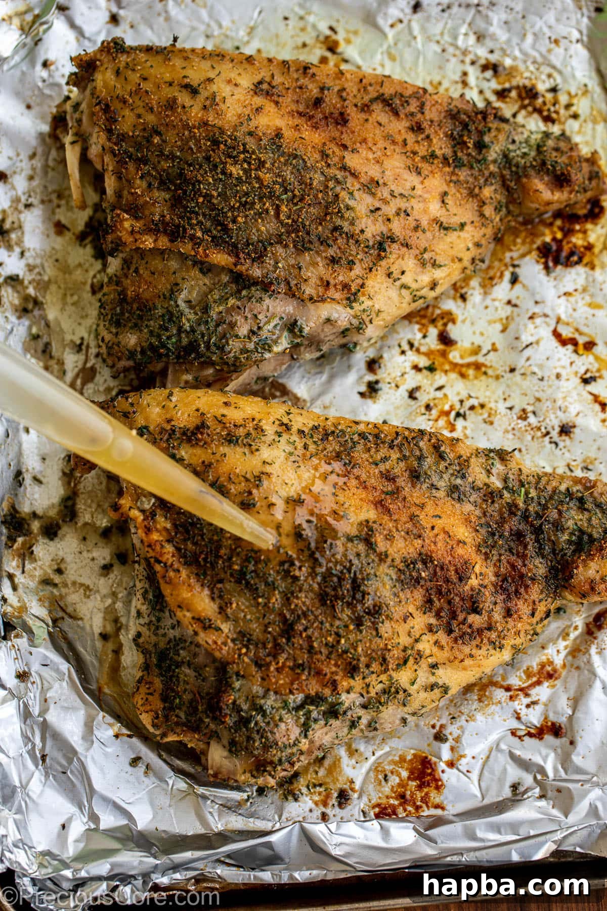 A hand basting over a turkey thigh with pan drippings during roasting.