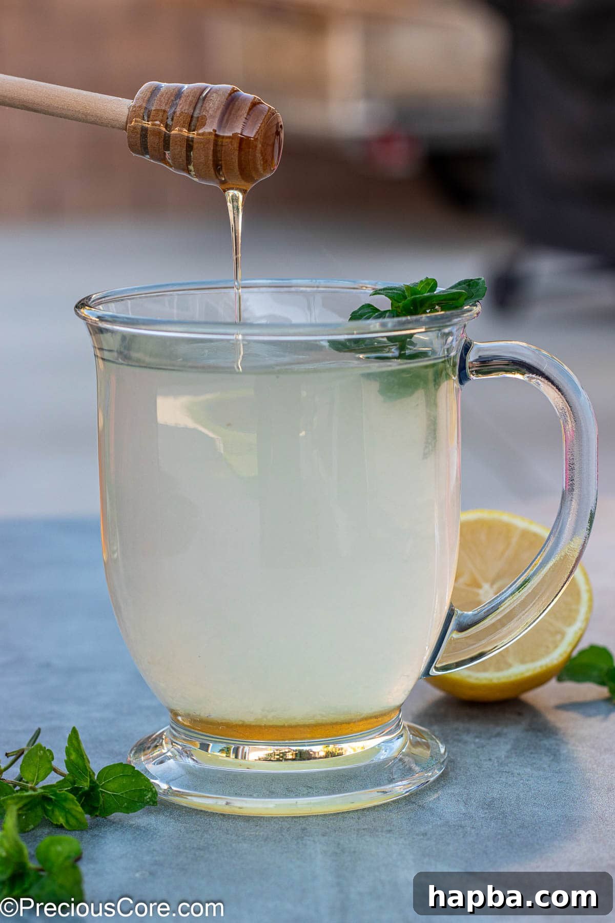 Honey dipper dripping golden honey into a steaming cup of freshly made honey lemon tea, ready to soothe.