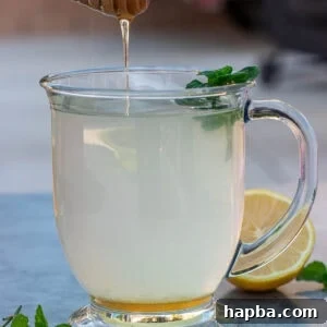 Honey dipper dripping honey into a cup of honey lemon tea.