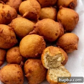 A platter brimming with golden-brown banana fritters, with one broken open to reveal its soft, fluffy interior.