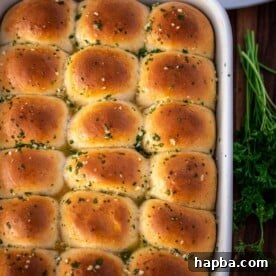 A baking dish filled with golden-brown, fluffy dinner rolls, generously brushed with aromatic garlic butter.