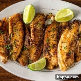 Golden brown pan-seared tilapia fillets garnished with fresh lime wedges, served on a elegant platter.