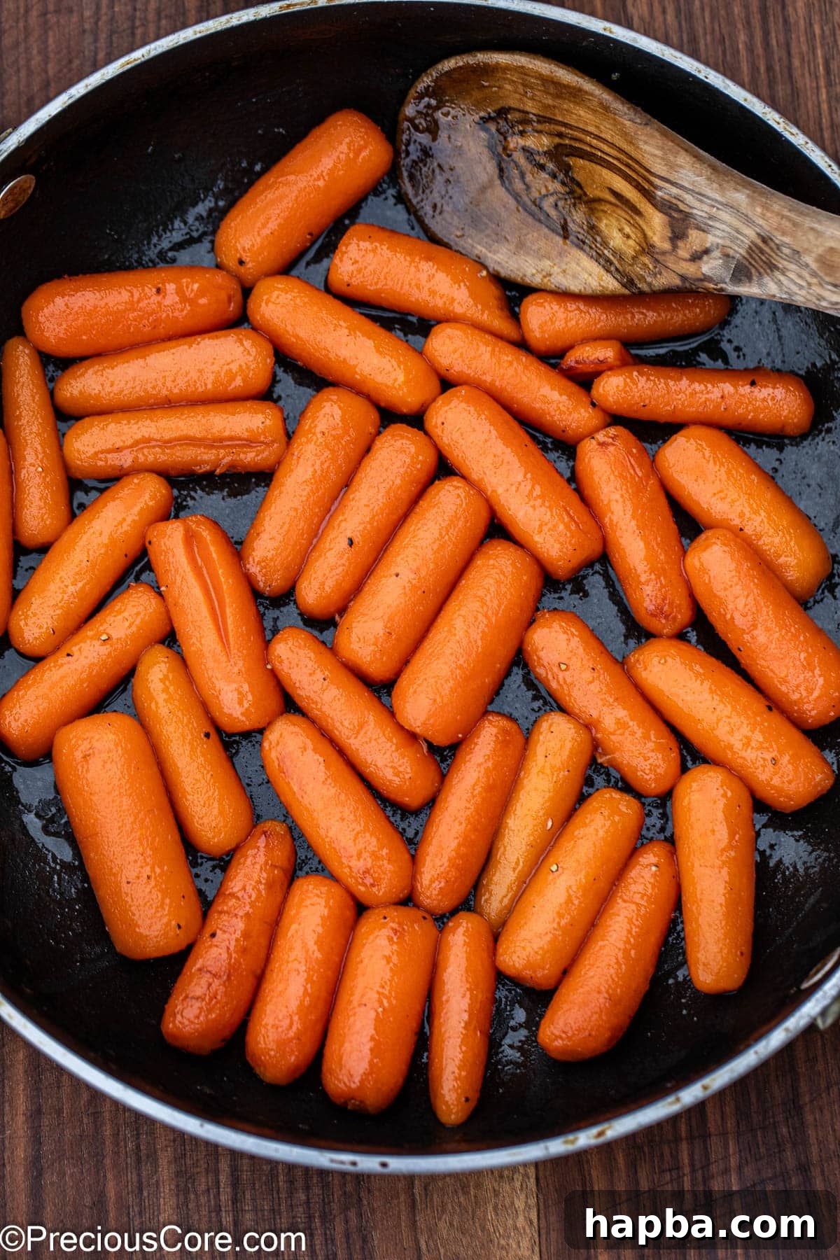 Honey glazed carrots simmering in a skillet, coated in a rich, shiny glaze.