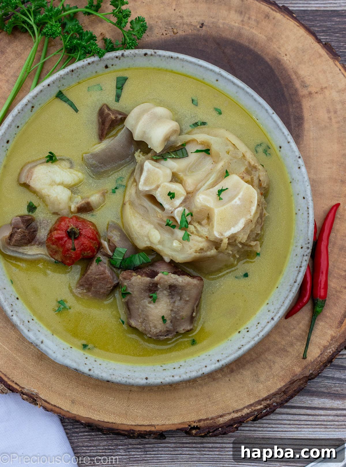 A large, inviting bowl of Cameroonian Pepper Soup, garnished with fresh herbs, sitting on a rustic wooden platter.