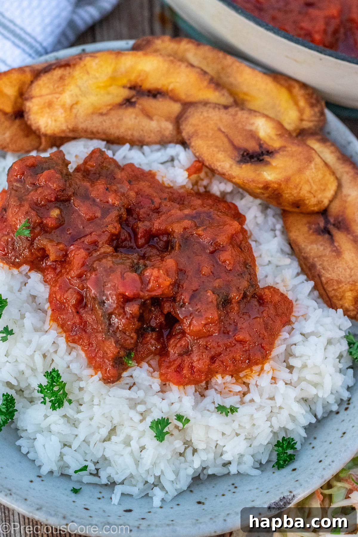 A bowl filled with steamed white rice, a generous portion of rich tomato stew, and perfectly fried plantains.