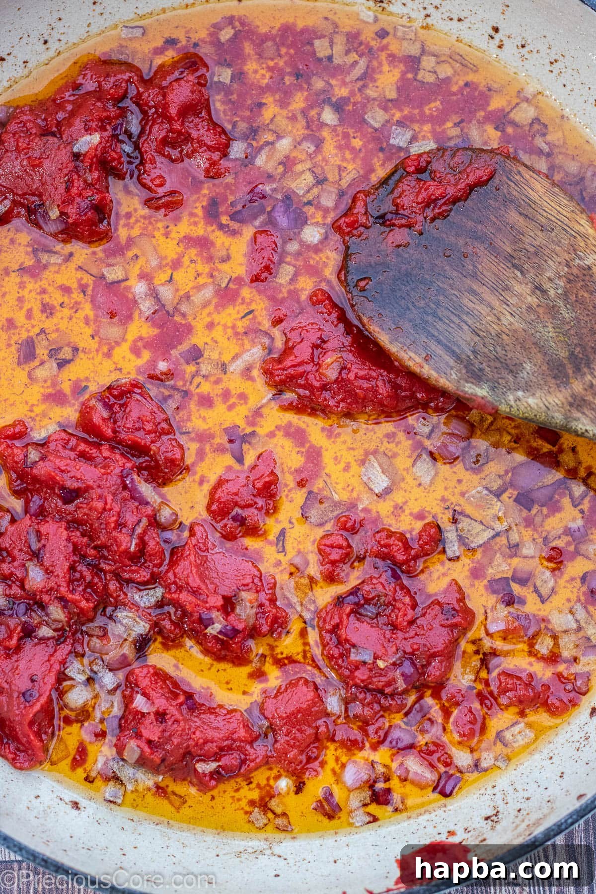 Diced onions sautéing with rich tomato paste in hot oil in a pot.
