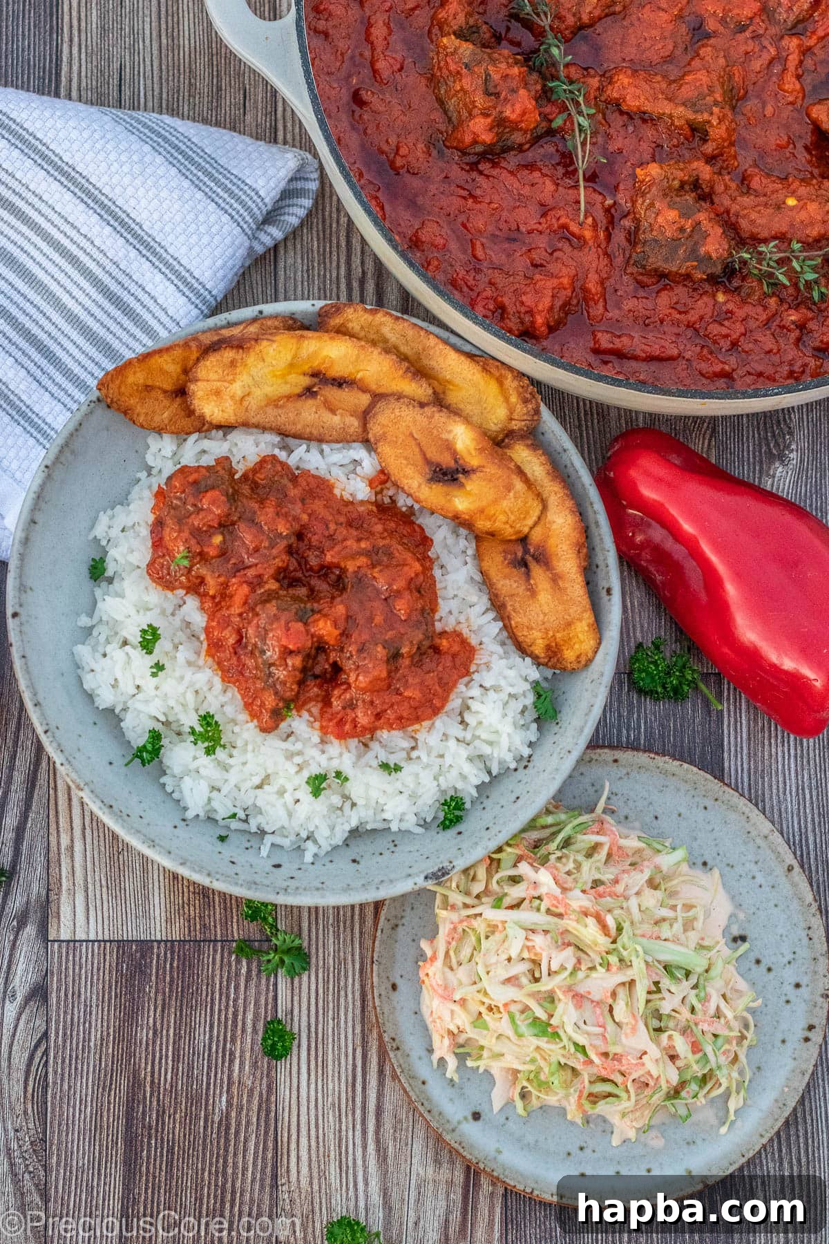 A serving of Nigerian beef stew accompanied by fluffy white rice, sweet fried plantains, and a refreshing side of coleslaw.