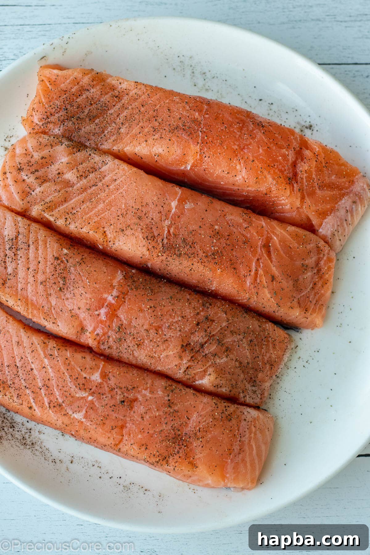 Zesty Lemon Butter Salmon 4 4 salmon fillet on a white plate, seasoned with salt and pepper.
