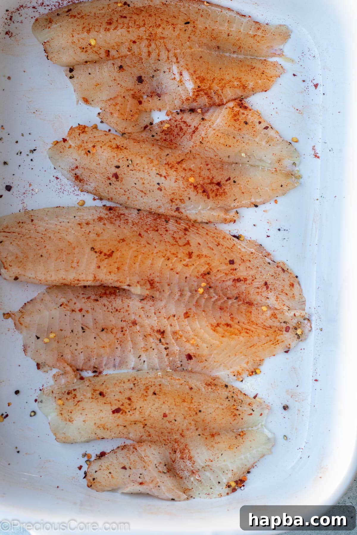 Seasoned tilapia fillets resting in a bowl, coated evenly with spices.