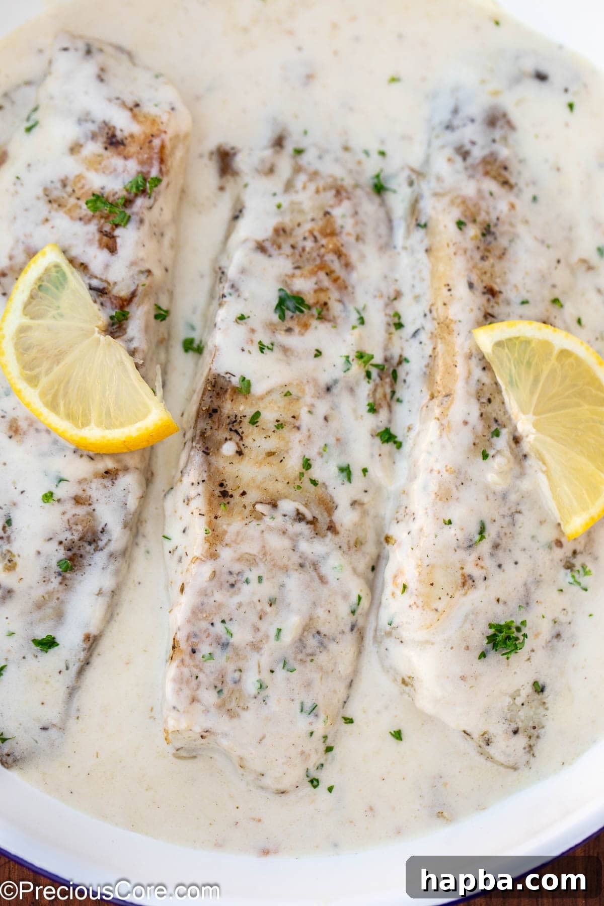 Creamy White Sauce Fish 2 Cooked fish fillets in a skillet with white sauce, garnished with fresh parsley.