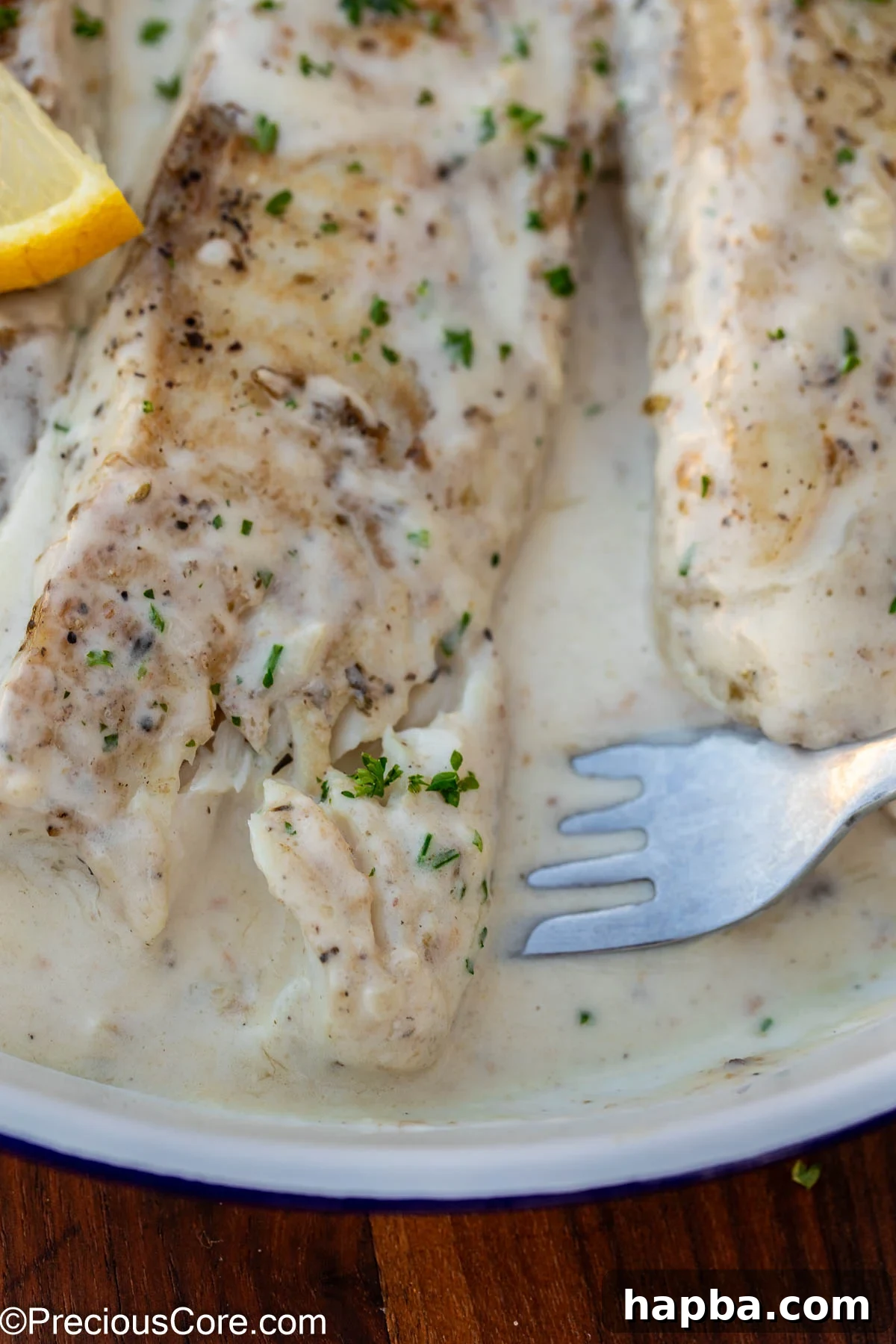 Creamy White Sauce Fish 3 A fork dipping into a piece of fish coated in white sauce, showing its tenderness.