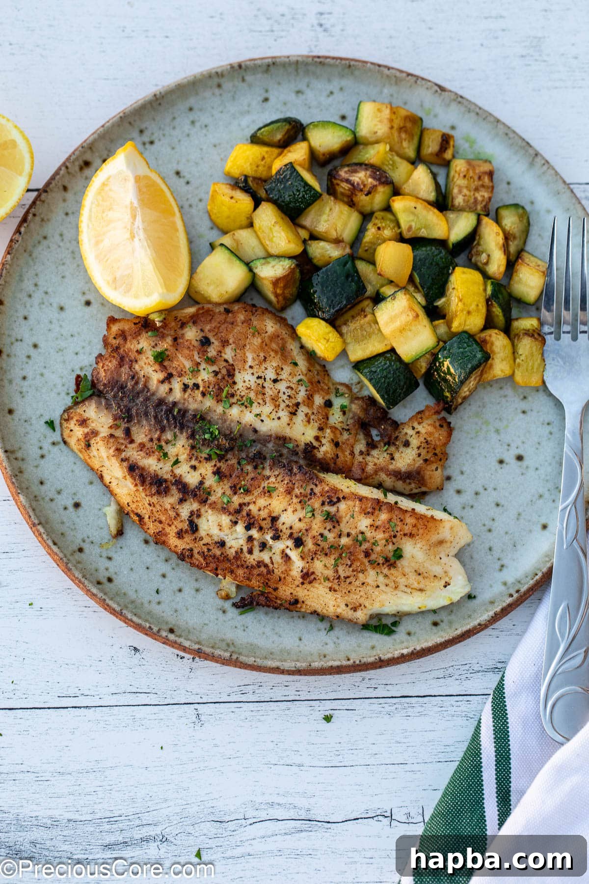 Zesty Lemon Pepper Tilapia 2 Lemon pepper tilapia on a plate with sautéed zucchini.