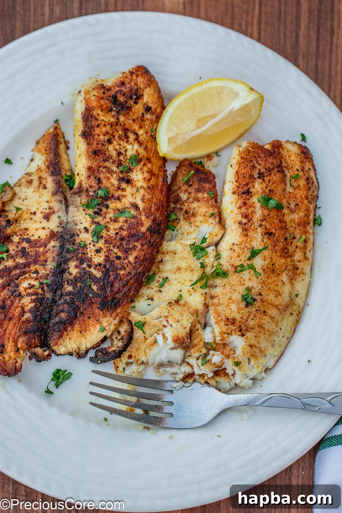 Zesty Lemon Pepper Tilapia 3 2 lemon pepper tilapia fillets on a white plate.