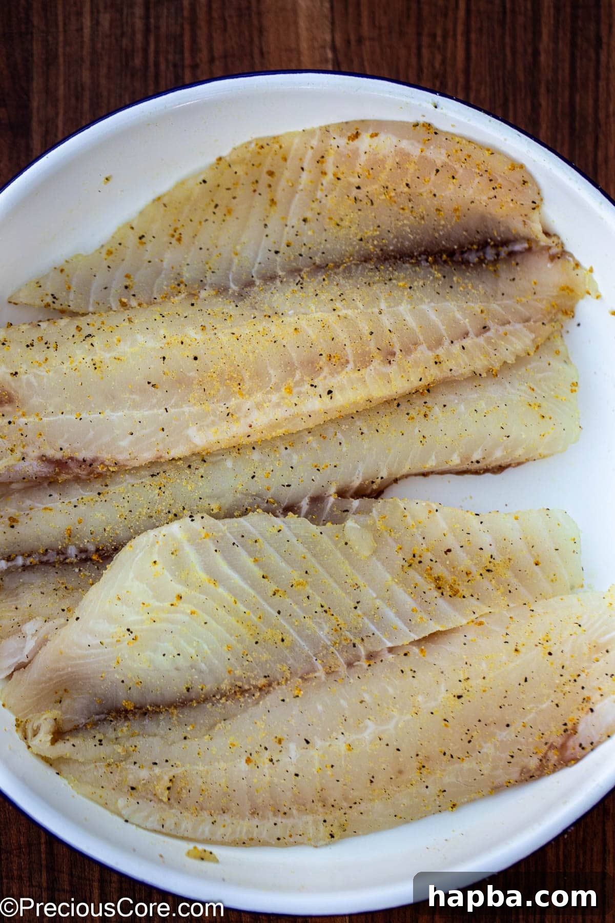 Zesty Lemon Pepper Tilapia 5 Seasoned tilapia fillets in a white bowl.