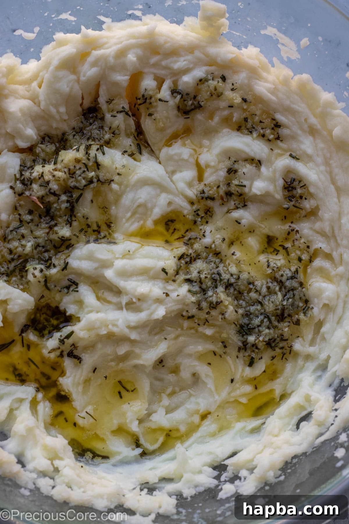 Melted butter and minced garlic and rosemary over mashed potatoes in a bowl.