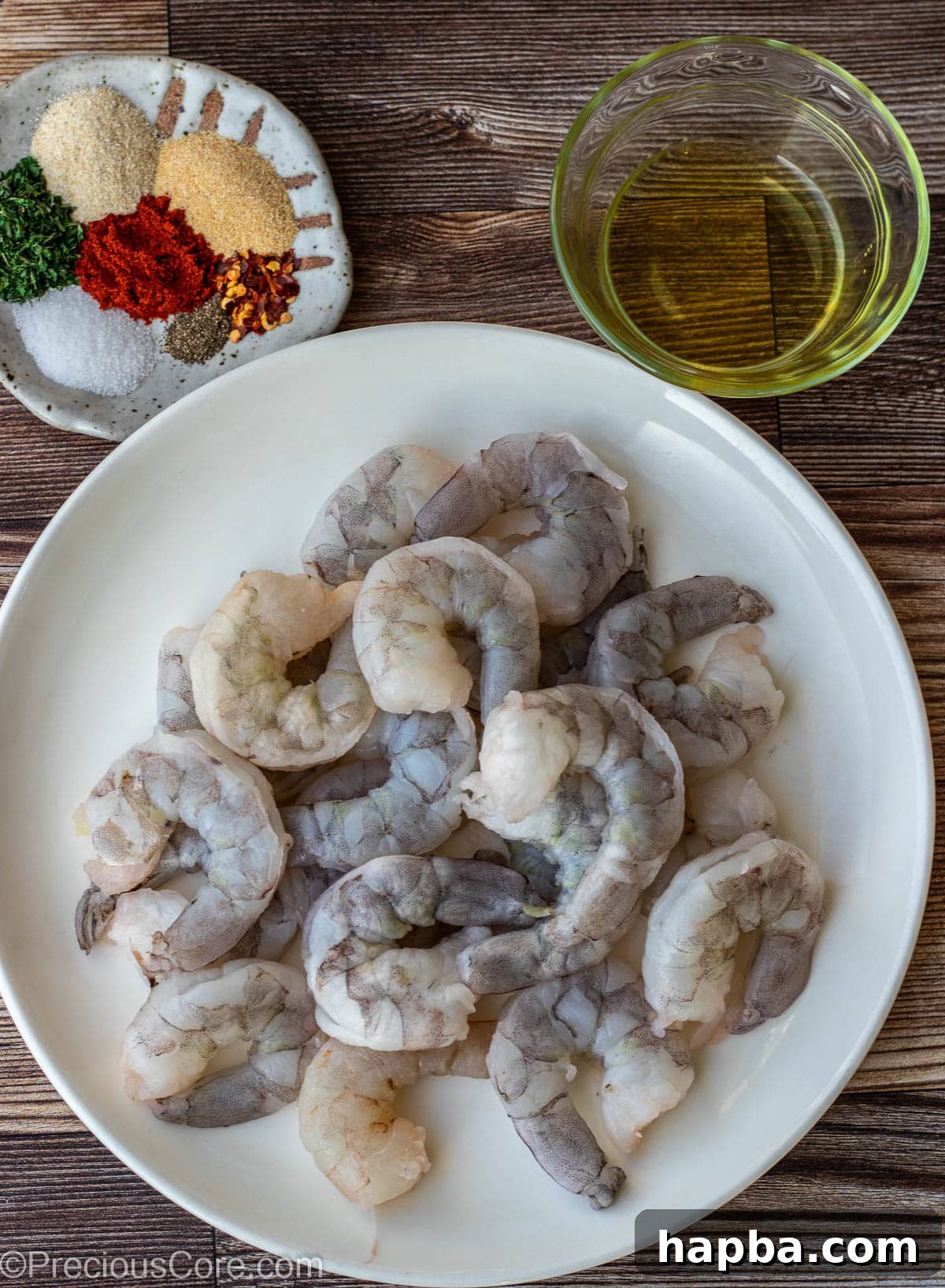 Raw shrimp on a plate, dried seasoning blend on a small dish, and olive oil in a bowl.