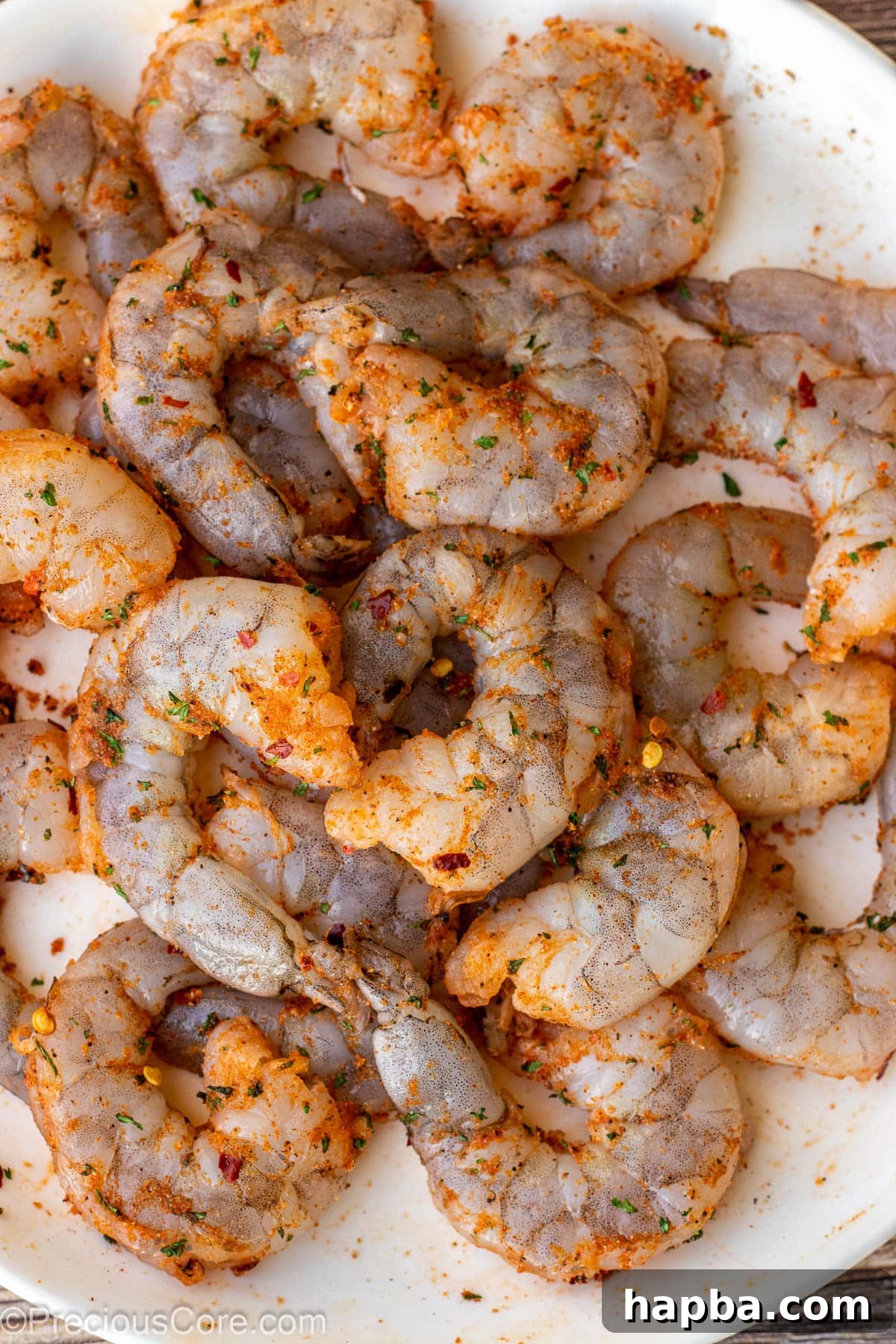 Raw seasoned shrimp ready for cooking on a white plate.