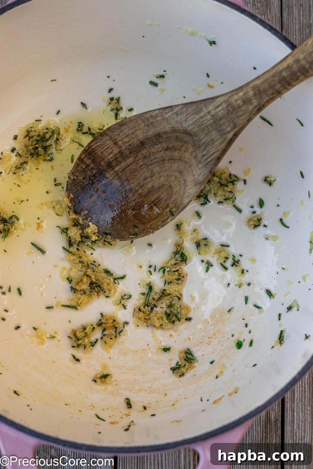 Fresh garlic, rosemary, and thyme gently sautéing in olive oil within a sturdy cast iron enamel pot, releasing their fragrant aromas.