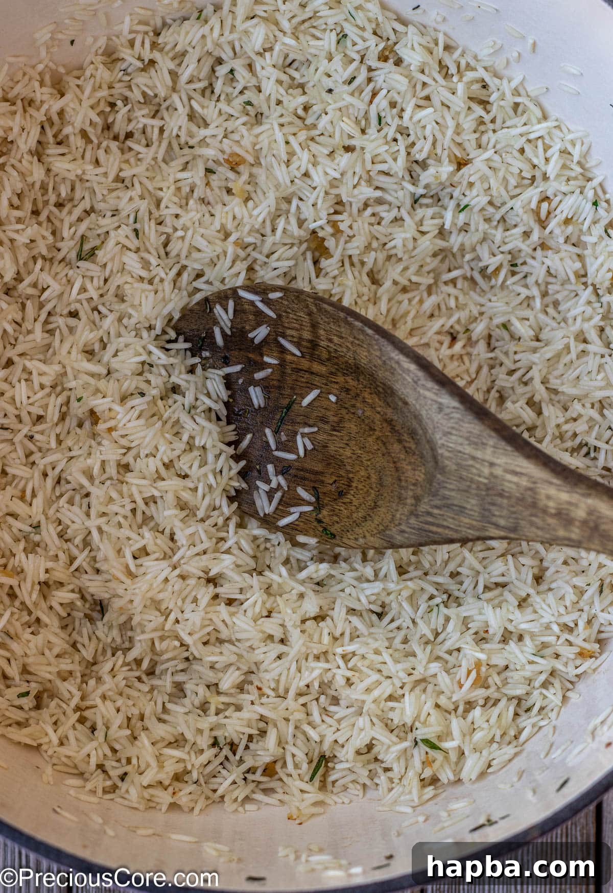 Rice being toasted to a light golden hue in a pot, absorbing the flavors of the previously sautéed herbs and garlic.