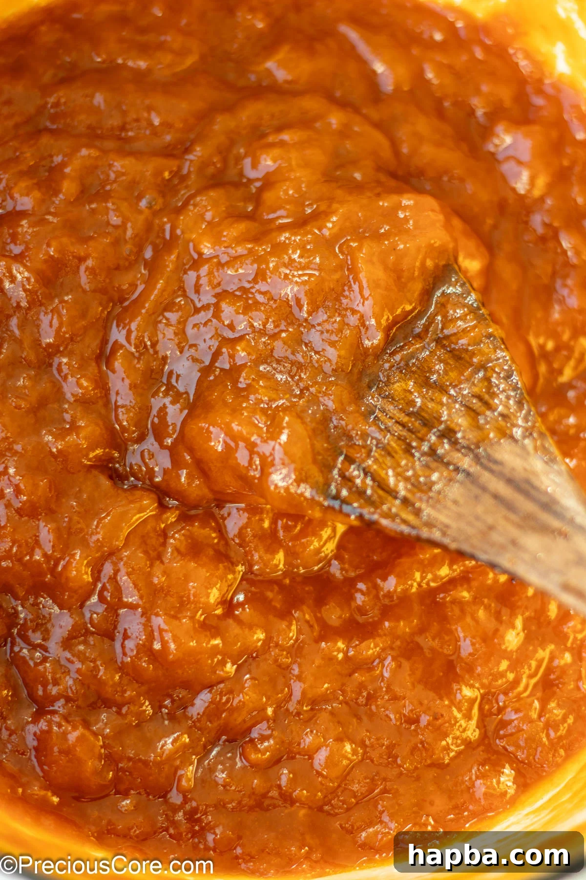 Sunshine Apricot Spread 10 A pot filled with fully cooked, rich apricot preserves, with a wooden spoon resting inside, showcasing its thick consistency.
