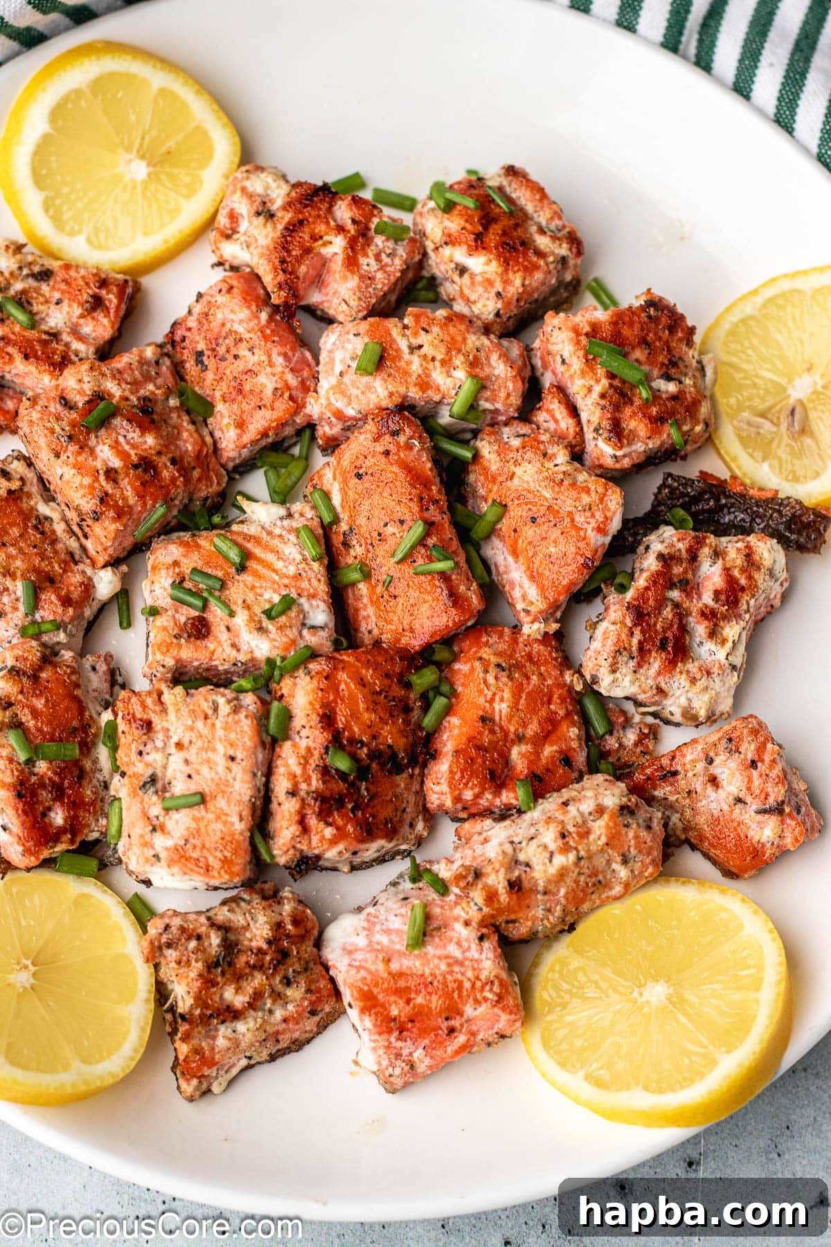 Crispy Salmon Bites 8 Golden-brown salmon bites on a white plate, elegantly garnished with fresh lemon slices and herbs.