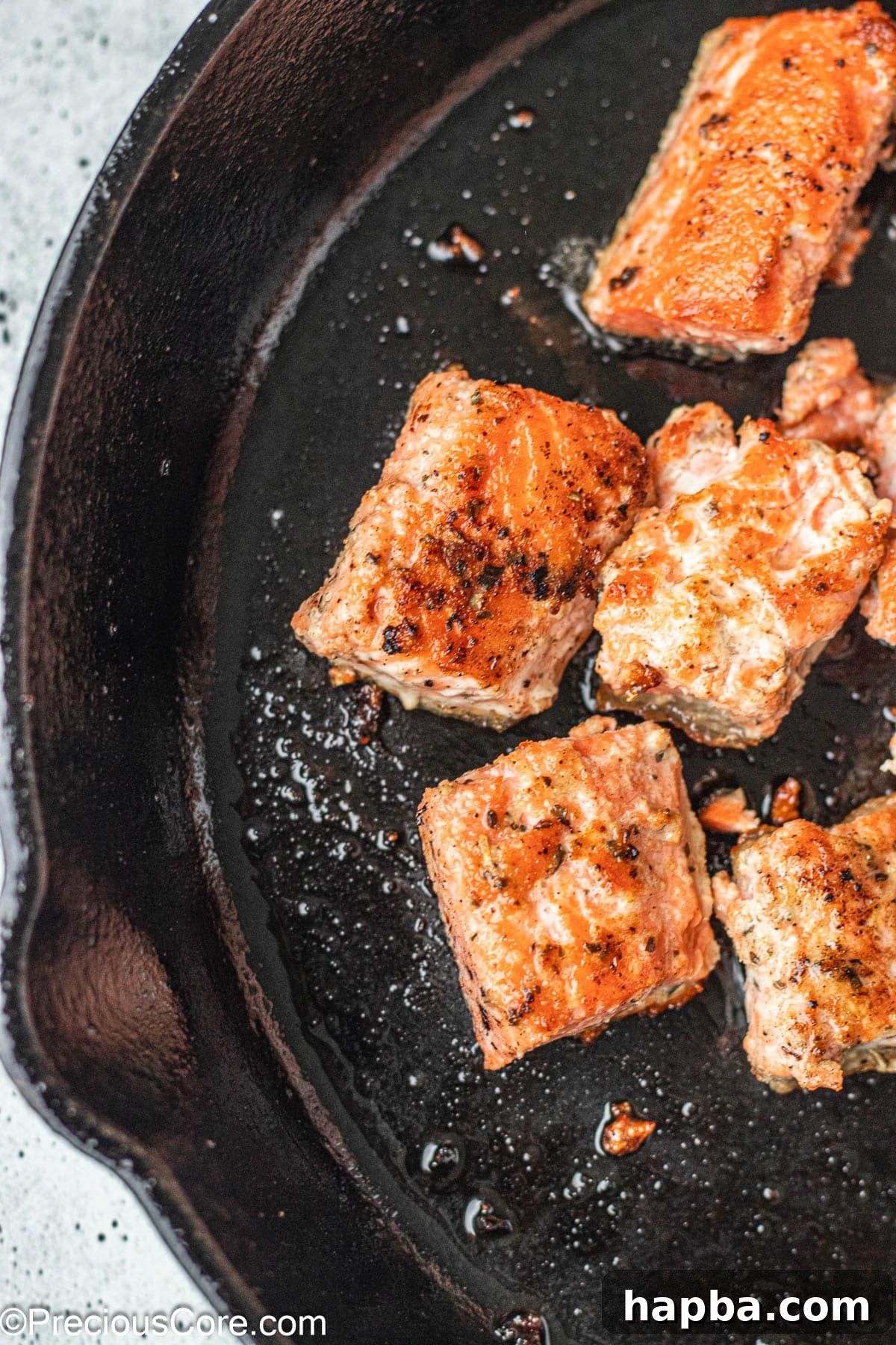 Crispy Salmon Bites 3 Salmon bites searing beautifully in a cast iron skillet.