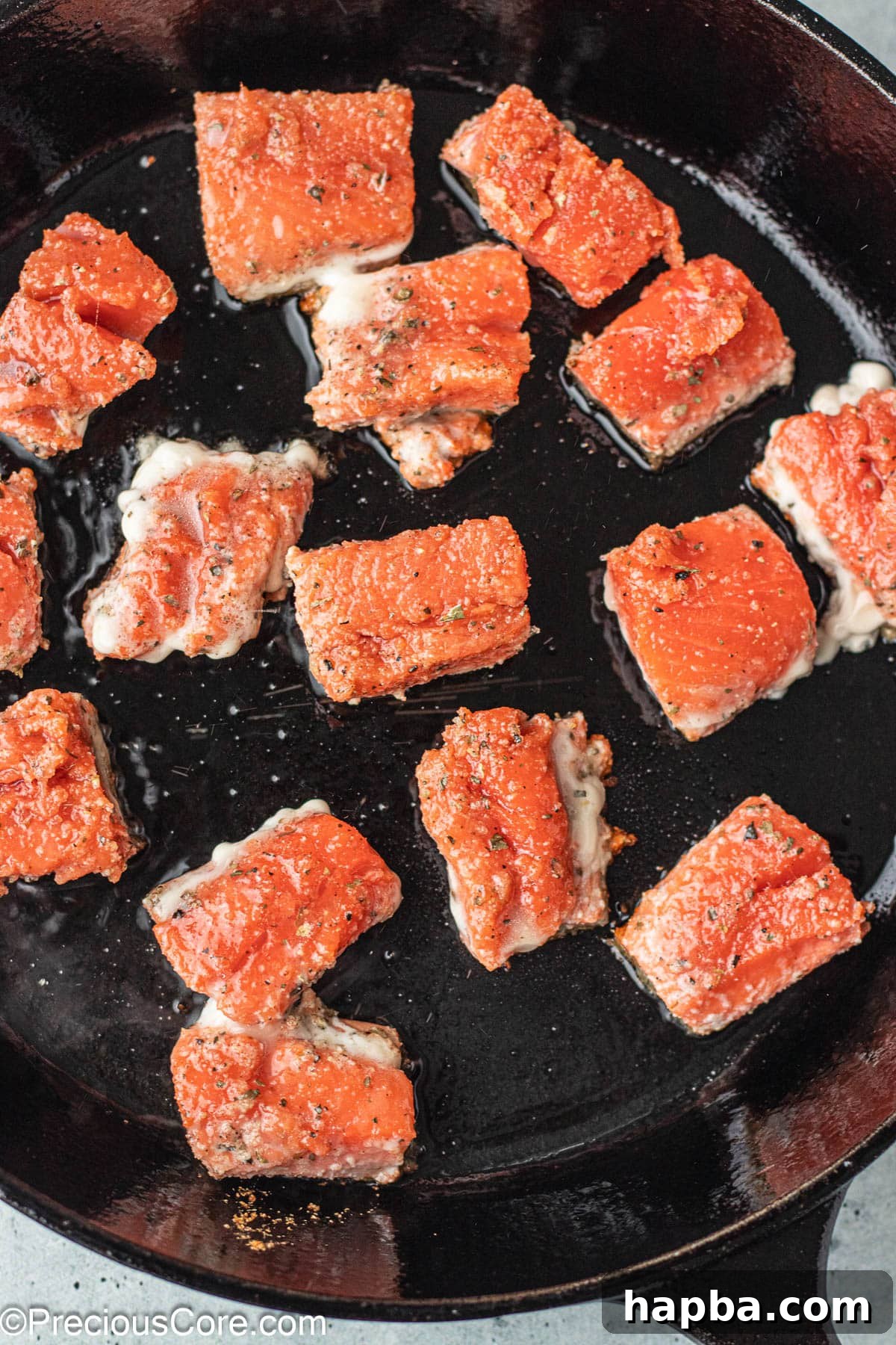 Crispy Salmon Bites 7 Salmon bites searing to a golden brown in a cast iron skillet.