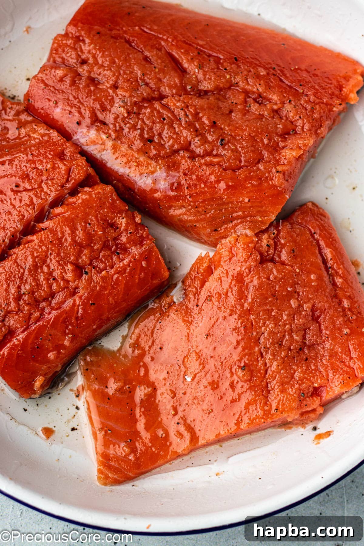 Raw salmon steaks in a white bowl, generously seasoned with olive oil, salt, and pepper.