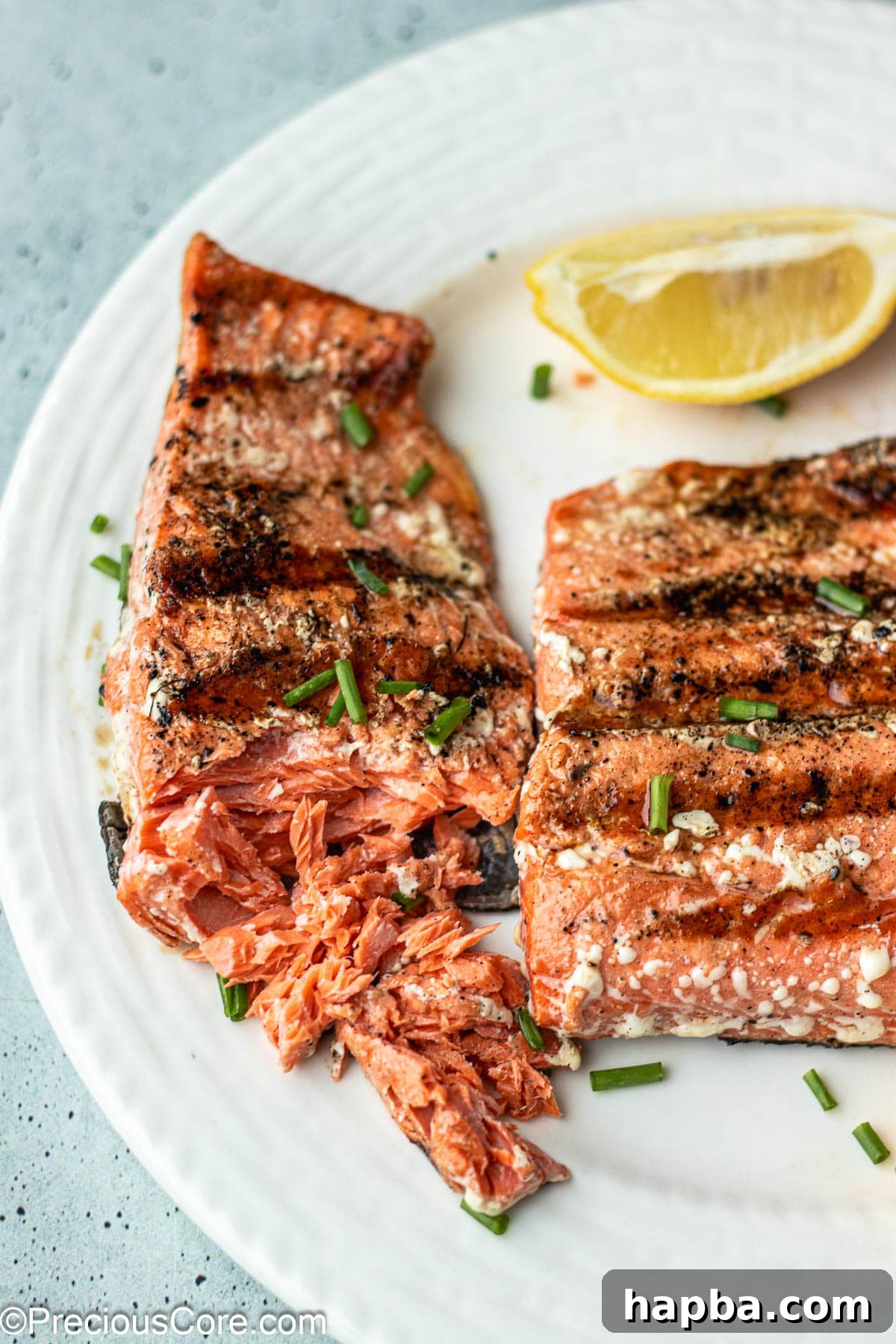 Two grilled salmon fillets on a plate, with one piece gently flaked with a fork to show its perfect doneness.