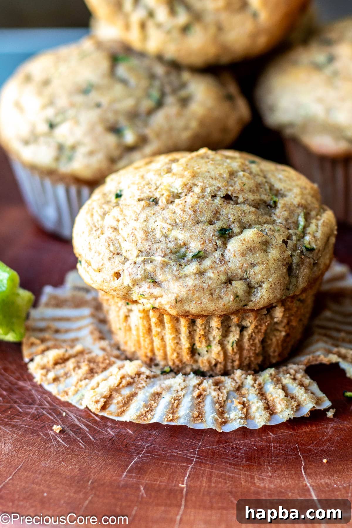 Wholesome Zucchini Applesauce Muffins 13 A single zucchini muffin in the foreground, with its paper lining partly peeled away, showing its golden crust and moist interior.