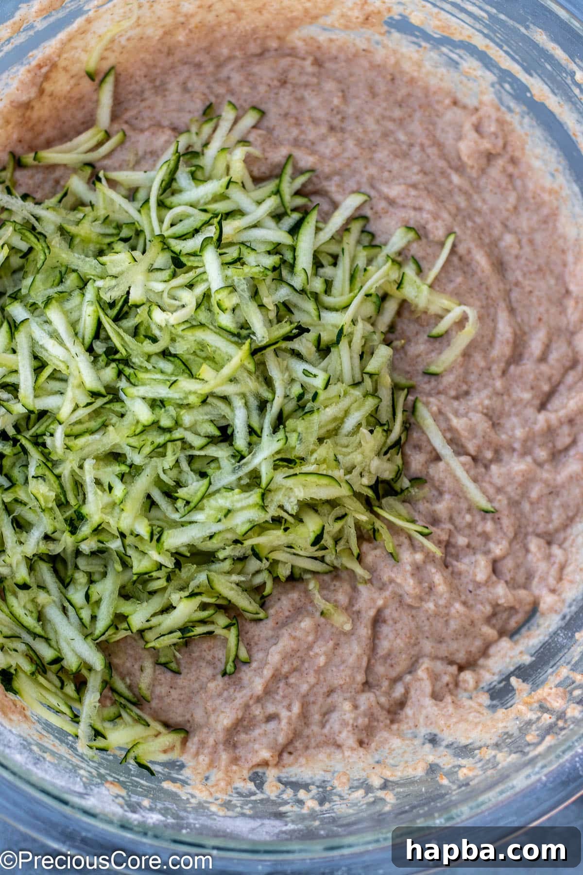 Wholesome Zucchini Applesauce Muffins 9 Shredded zucchini being gently added to the prepared muffin batter in a large mixing bowl.