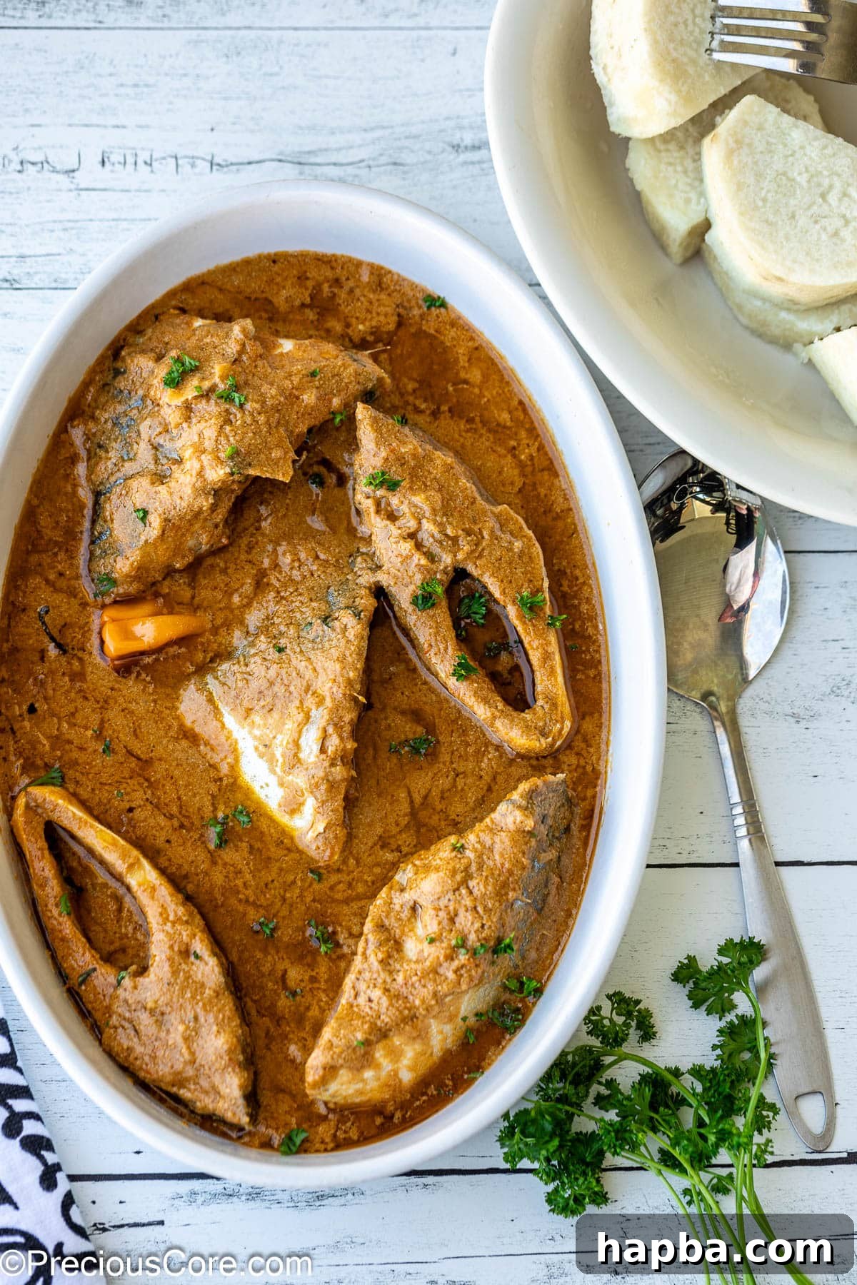 Njangsa sauce in a white oval bowl with white yams on the side, highlighting the creamy texture and vibrant presentation.