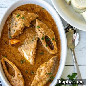 Njangsa sauce in a white oval bowl with white yams on the side, a vibrant and creamy Cameroonian dish.