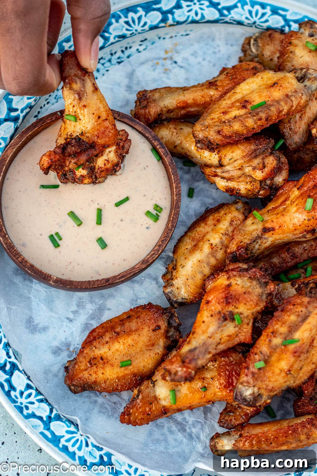 Crispy Baked Dry Rub Wings 3 A crispy baked dry rub chicken wing being dipped into a bowl of creamy ranch dressing, highlighting its golden texture.