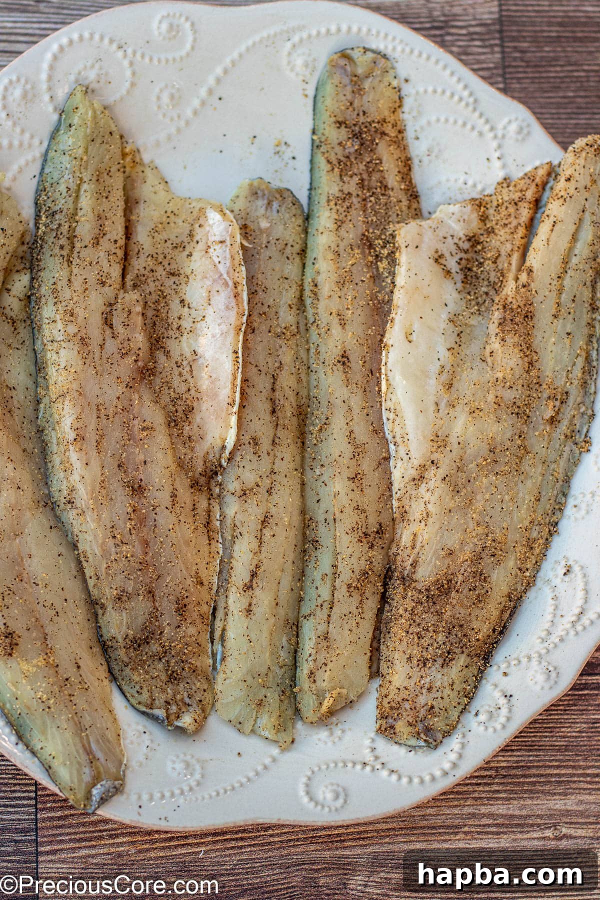 Crispy-Skinned Sea Bass 5 Sea bass fillets evenly seasoned with salt, pepper, garlic powder, and onion powder on a large plate, ready for searing.