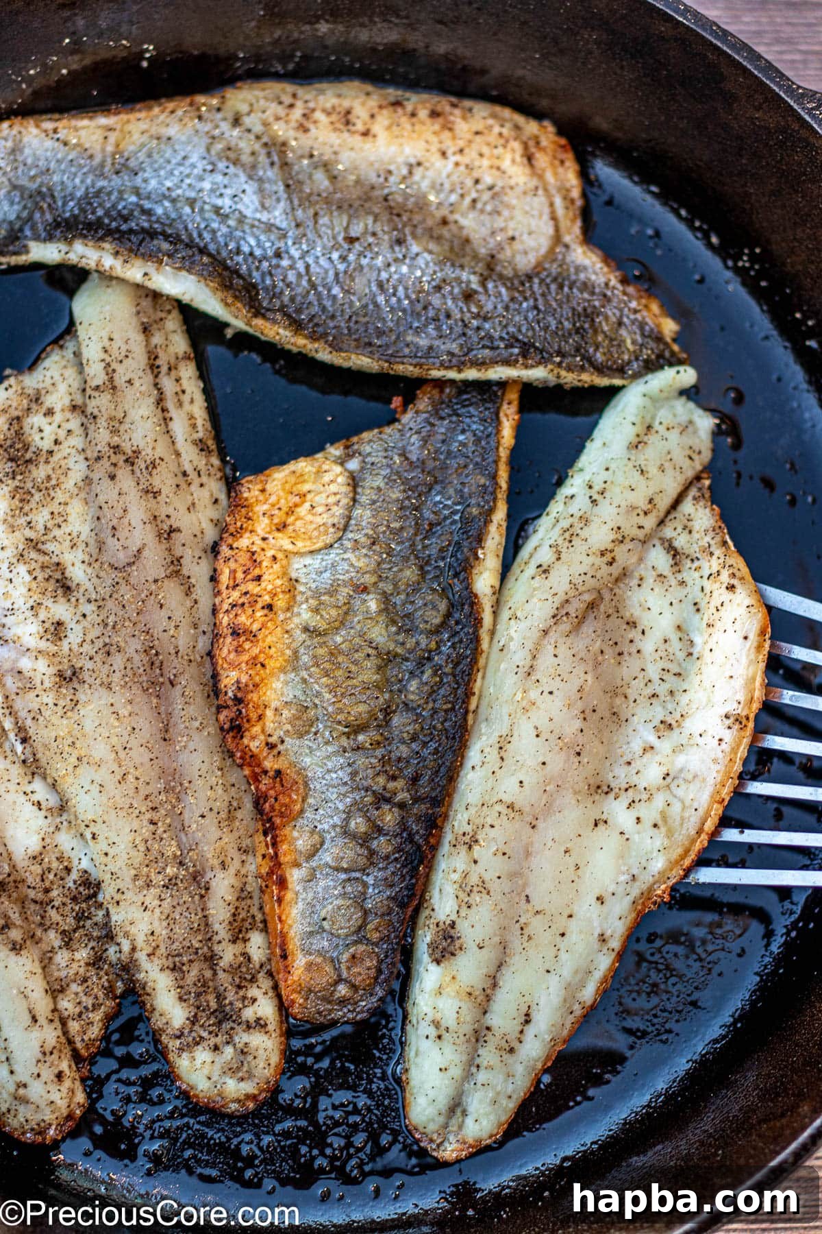 Crispy-Skinned Sea Bass 7 A fish spatula carefully flipping a pan-seared sea bass fillet in a skillet, showcasing its perfectly golden-brown and crispy crust.