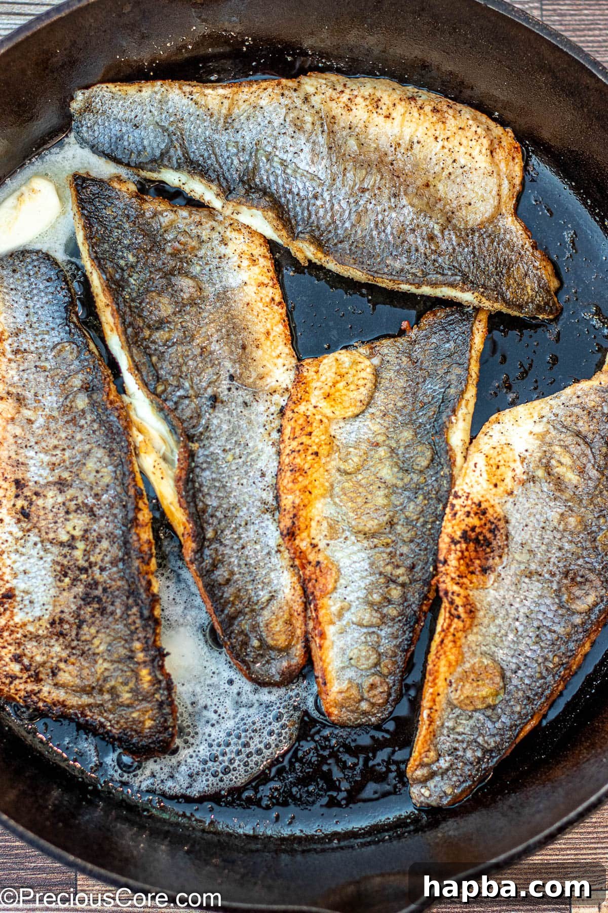 Crispy-Skinned Sea Bass 8 Butter melting and bubbling in a hot cast iron skillet alongside pan-seared sea bass fillets, creating a luscious sauce.