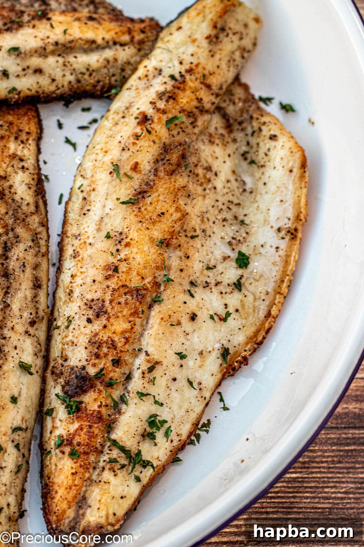 Crispy-Skinned Sea Bass 9 Beautifully pan-seared sea bass garnished with fresh minced parsley and lemon wedges on a white plate, ready for a gourmet meal.