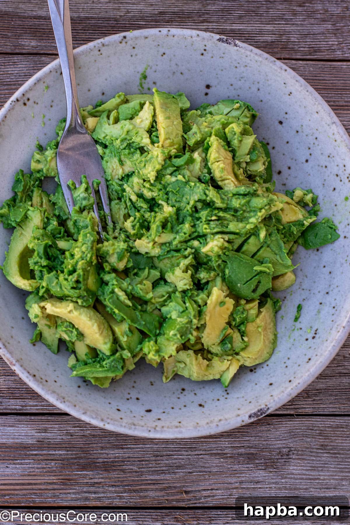 Effortless 4 Ingredient Guacamole 7 Hands using a fork to mash avocados in a bowl, demonstrating the mashing process.
