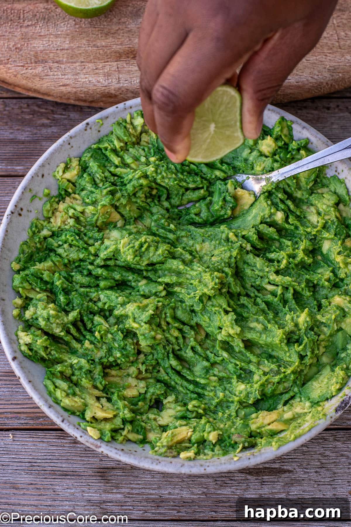 Effortless 4 Ingredient Guacamole 9 A hand squeezing fresh lime juice directly into a bowl of mashed avocados.