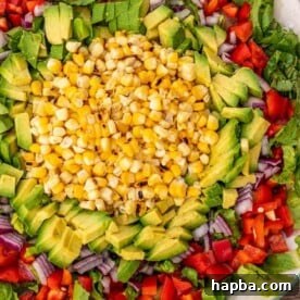 Corn, avocado, and other colorful vegetables arranged for a salad on a platter.