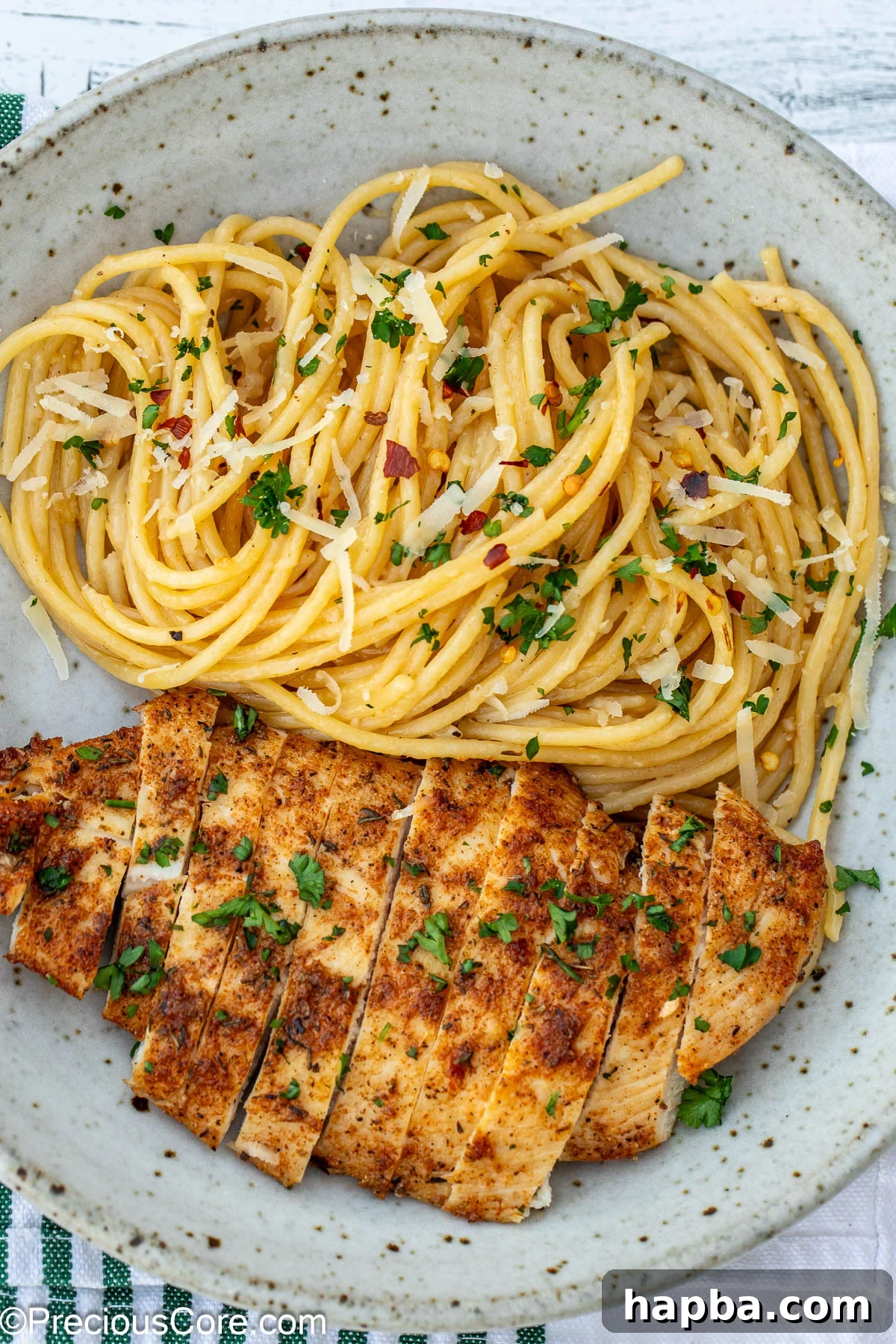 A generous serving of garlic butter pasta with golden seared chicken breasts in a white bowl, garnished with fresh herbs.