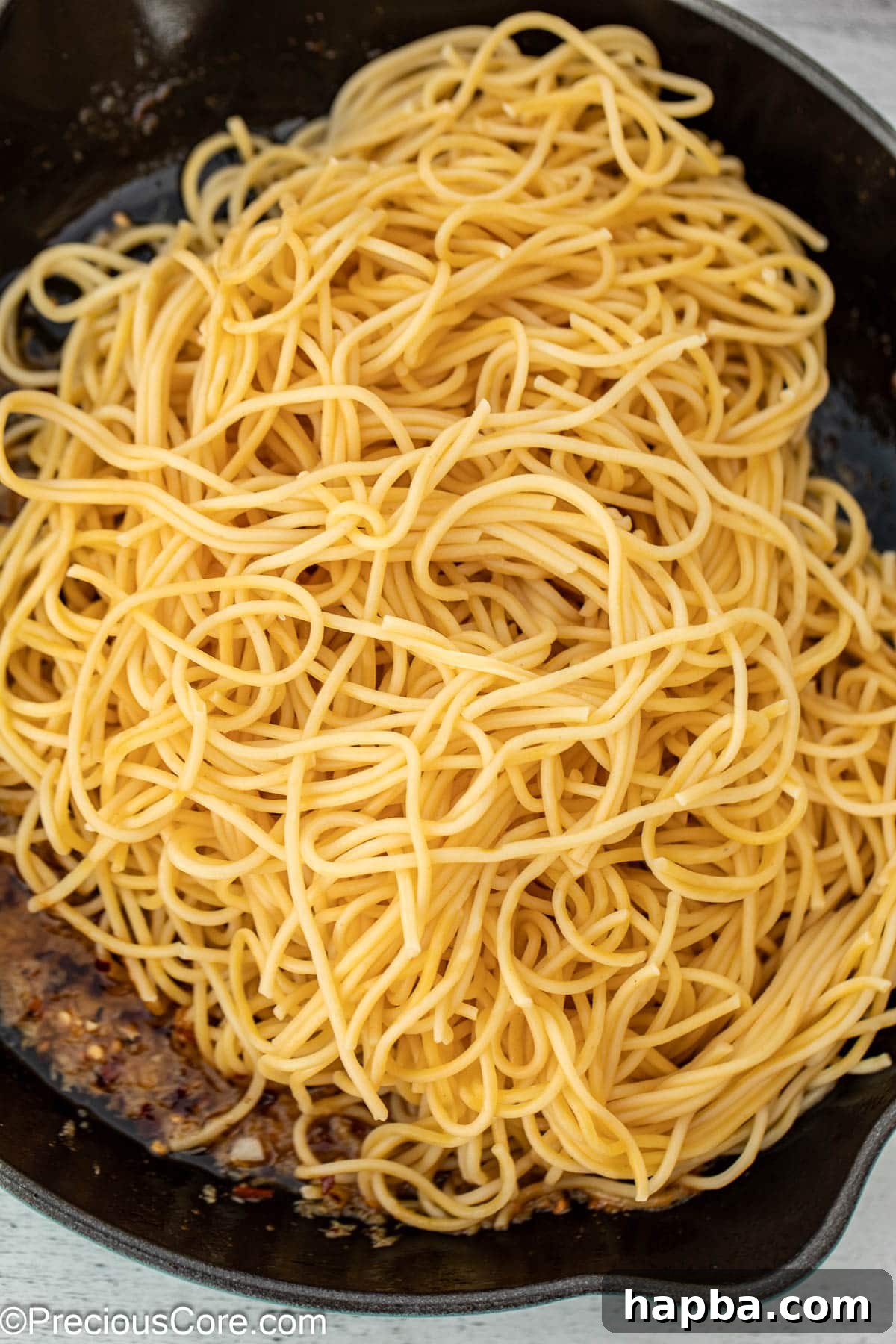 Cooked spaghetti noodles being added to a cast iron pan with the garlic butter sauce, ready to be tossed.