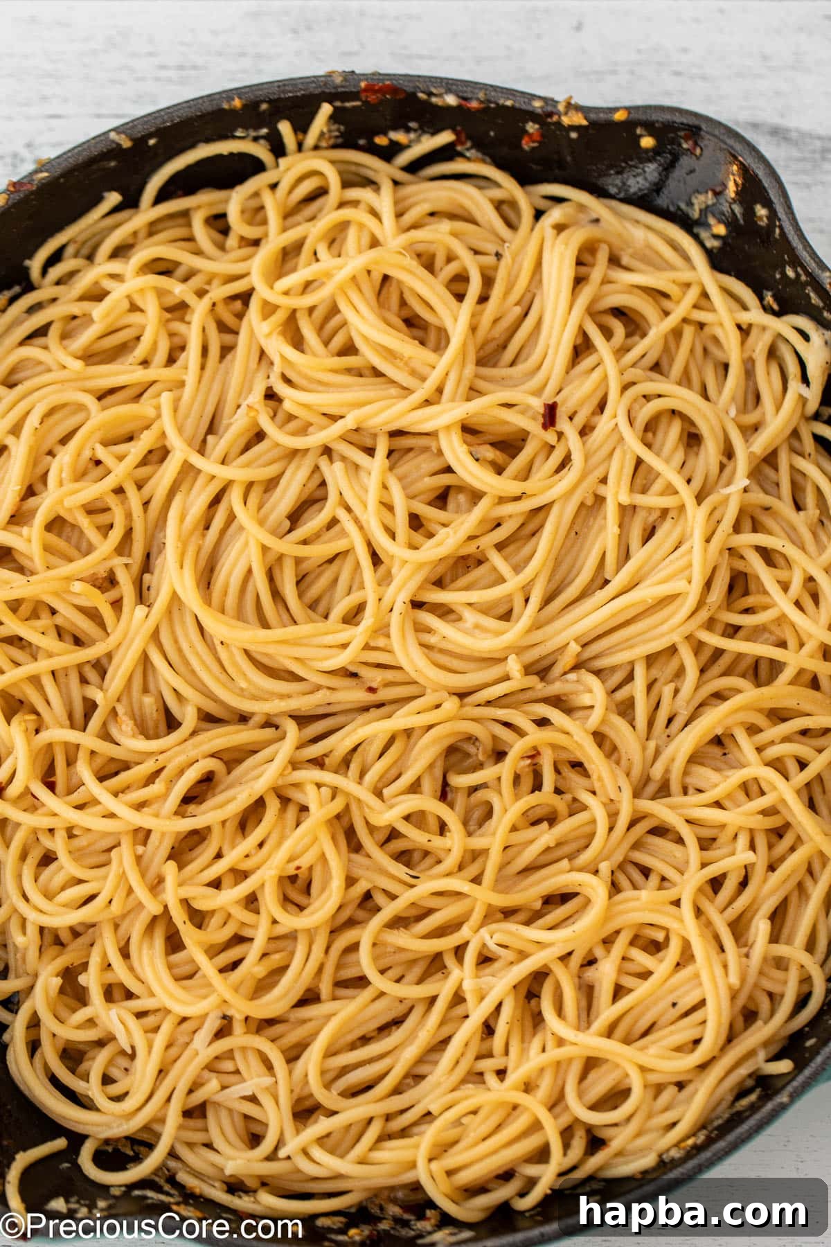 Spaghetti expertly tossed and coated in a glistening garlic butter sauce within a cast iron pan.