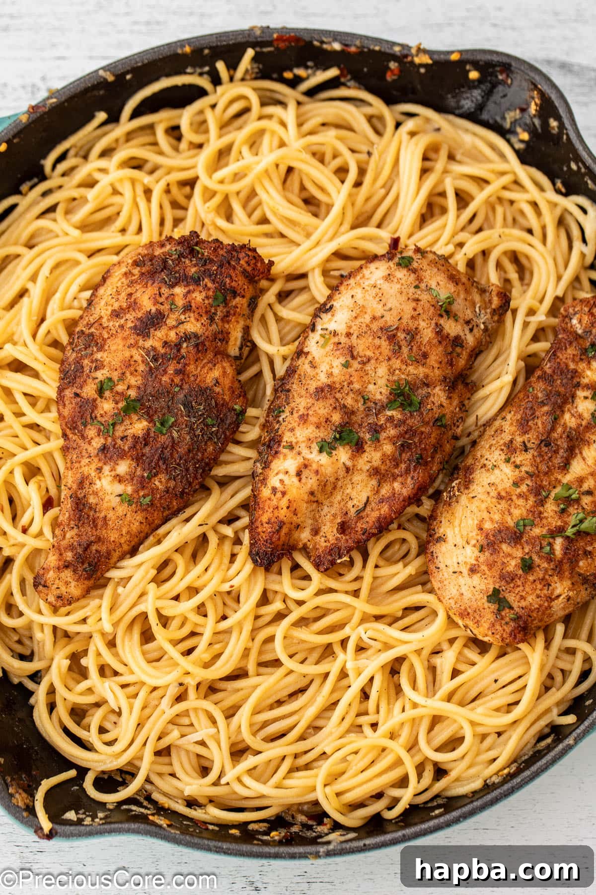 A rustic cast iron skillet filled with glossy garlic butter spaghetti, topped with sliced pan-seared chicken.