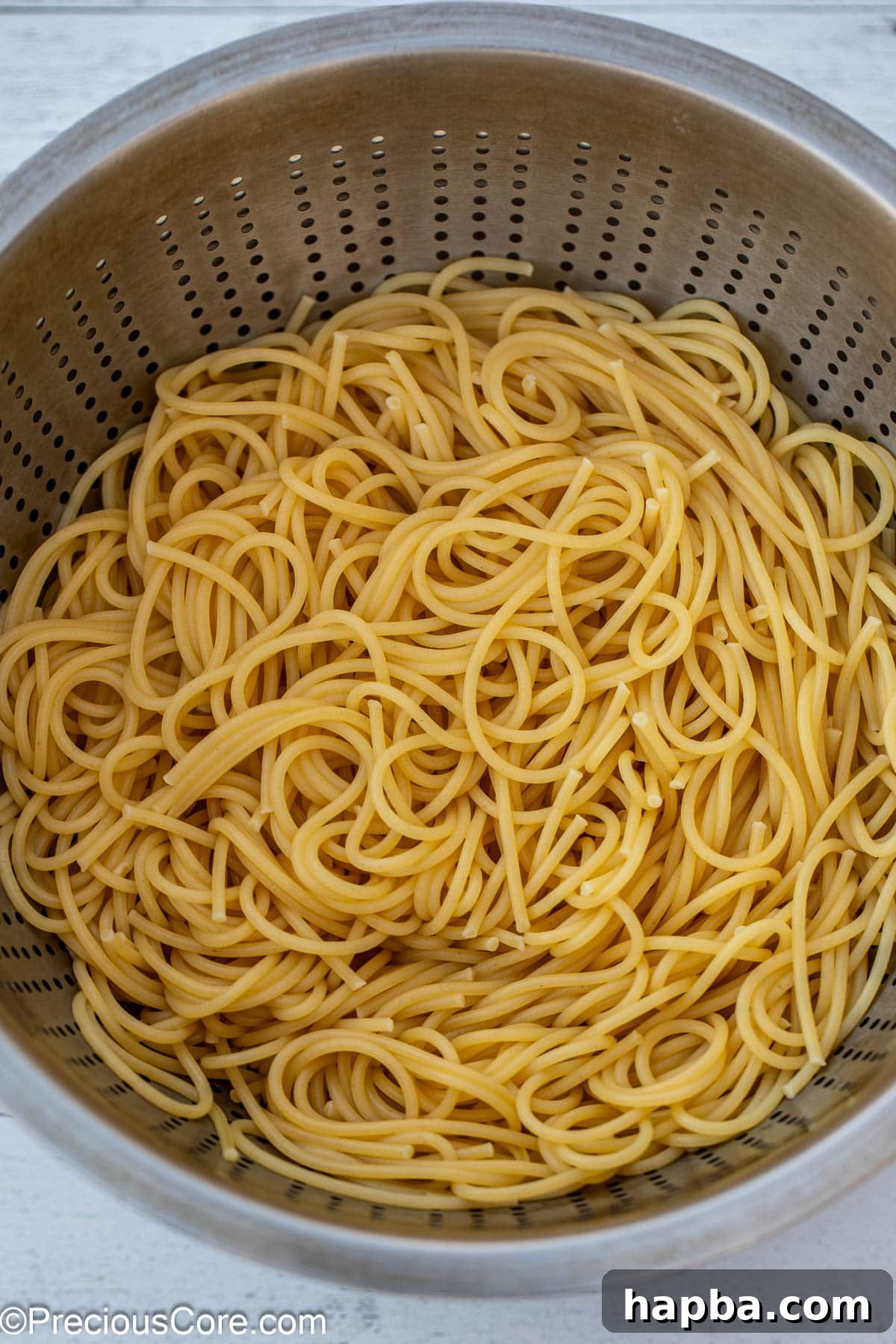 Freshly cooked and strained spaghetti noodles resting in a metal colander.