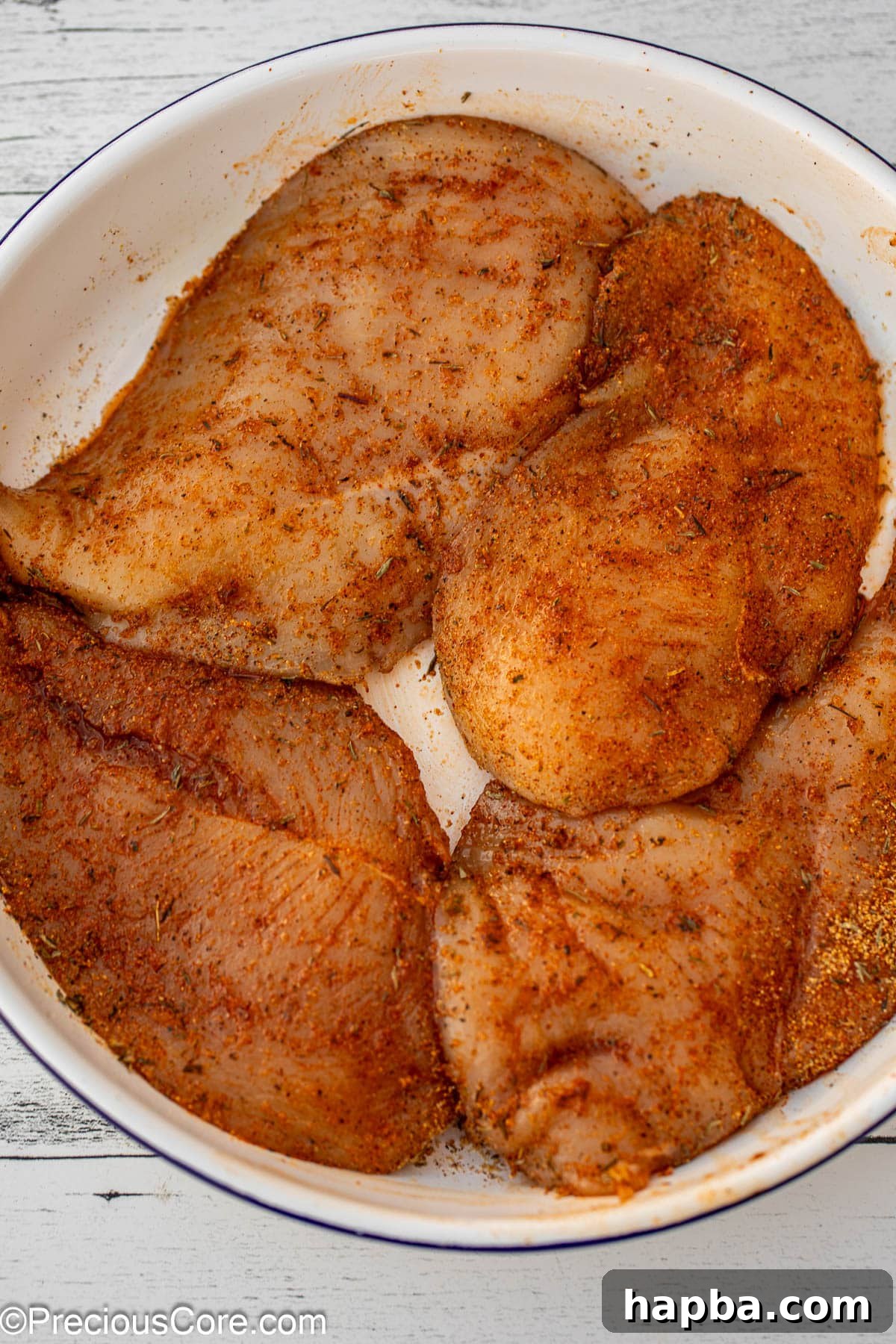 Thinly sliced raw chicken breasts seasoned generously with various spices, ready for cooking.