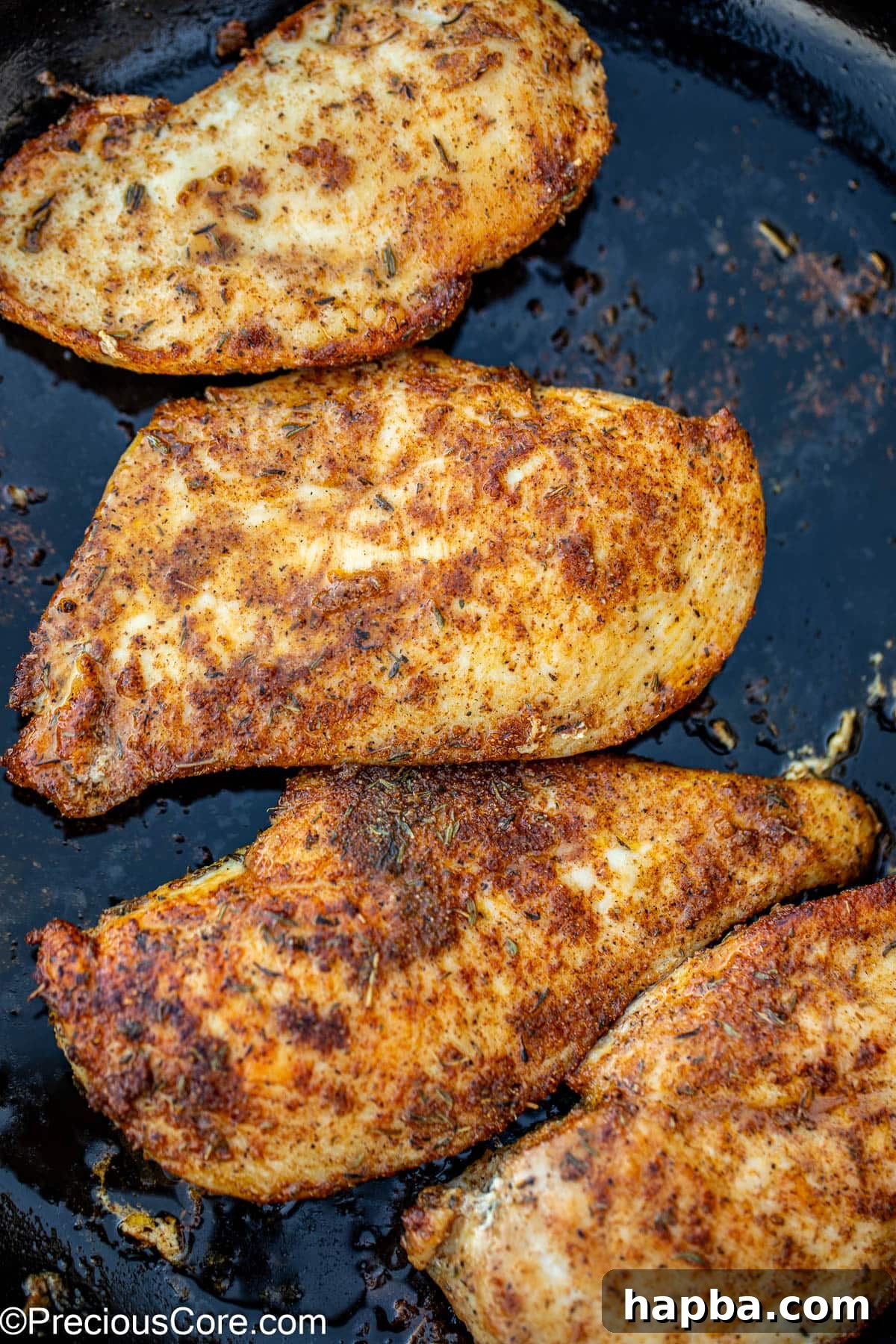 Two pieces of golden-brown pan-seared chicken breasts cooking in a hot skillet.